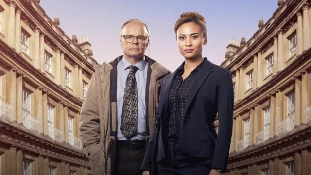 Twee mensen in zakelijke kleding staan voor een rij oude gebouwen bij zonsondergang.