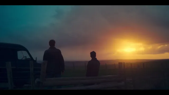 Twee personen staan bij een hek, kijken naar zonsondergang.