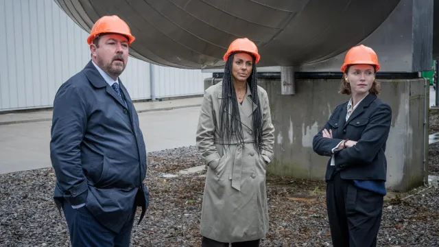 Drie mensen met een oranje helm op een bouwplaats