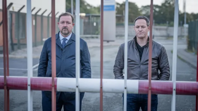 Twee mannen staan achter een hek