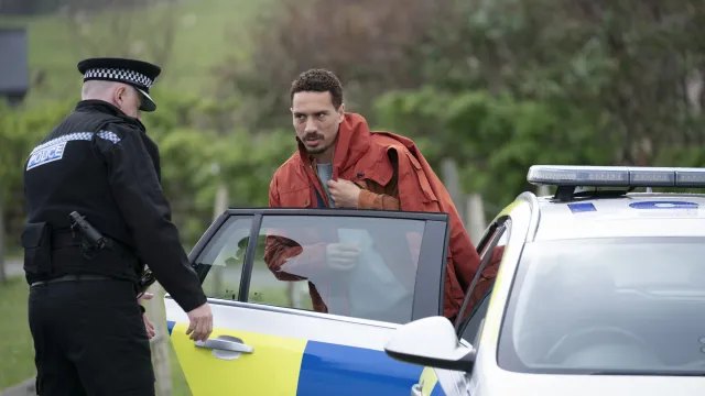 Een agent en een man staan naast een politieauto