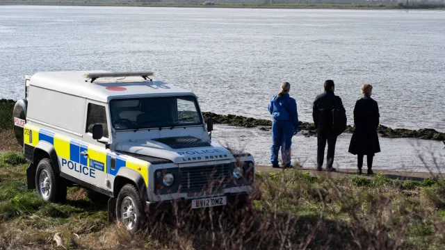 Een politie auto staat naast het water en drie mensen die over het water uitkijken