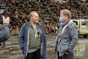 Op de set van de serie Wisting. Je ziet acteur Sven Nordin praten met iemand van de crew. Op de achtergrond staat een politiebusje.