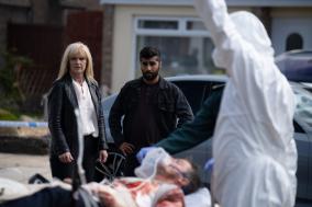 Vrouw en man kijken naar een gewonde op brancard, omgeven door hulpverleners.