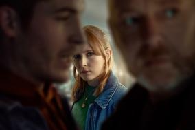 Een vrouw in een groene trui, kijkend tussen twee onscherpe mannen in de voorgrond.