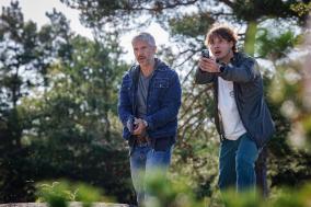 Twee mannen in een bos houden een pistool in de hand, alert kijkend.