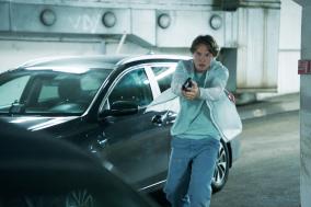 Persoon met pistool in een parkeergarage naast een auto.