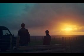 Twee personen staan bij een hek, kijken naar zonsondergang.