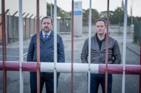 Twee mannen staan achter een hek