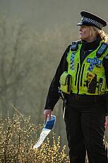 Vrouw in politie uniform staat in een groenrijk gebied, ze kijkt naar de zijkant. 