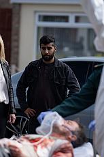 Vrouw en man kijken naar een gewonde op brancard, omgeven door hulpverleners.