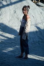 Vrouw in casual kleding staat op zand met schaduwen en zonlicht.