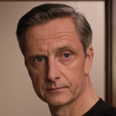 Man met grijzend haar kijkt serieus naar de camera.