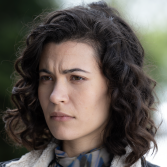 Vrouw met krullend haar kijkt serieus naar iets in de verte.