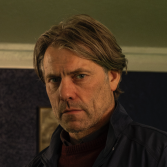 Verstarde man met donkerblond haar in donkere kamer.