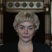 Vrouw met blond kapsel in formele omgeving, serieuze blik.