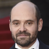 Man in smoking met baard, glimlachend, op rode loper.